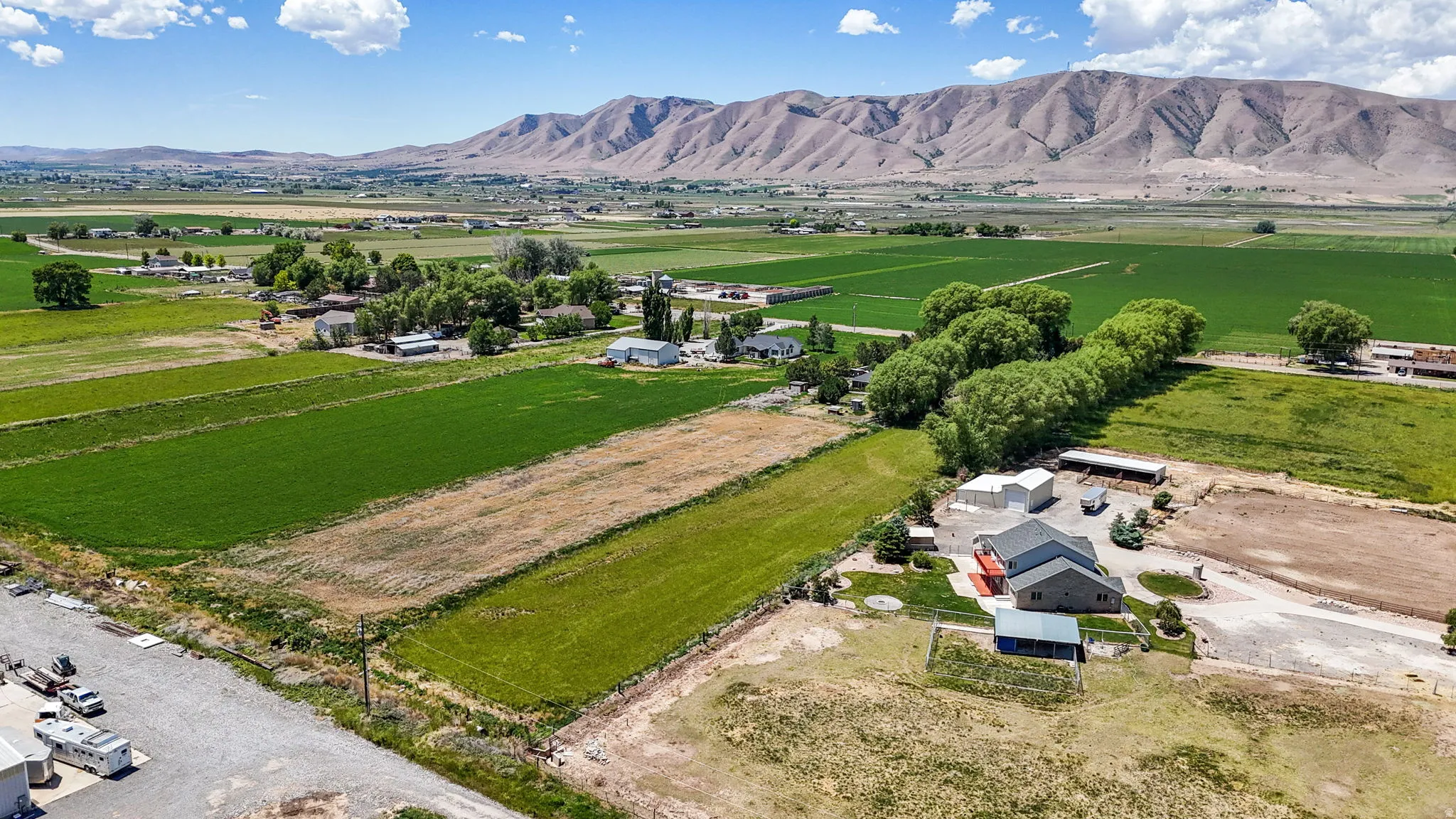 Expansive rural property featuring multiple agricultural fields, a primary residence with an attached garage, several outbuildings, and mature tree lines