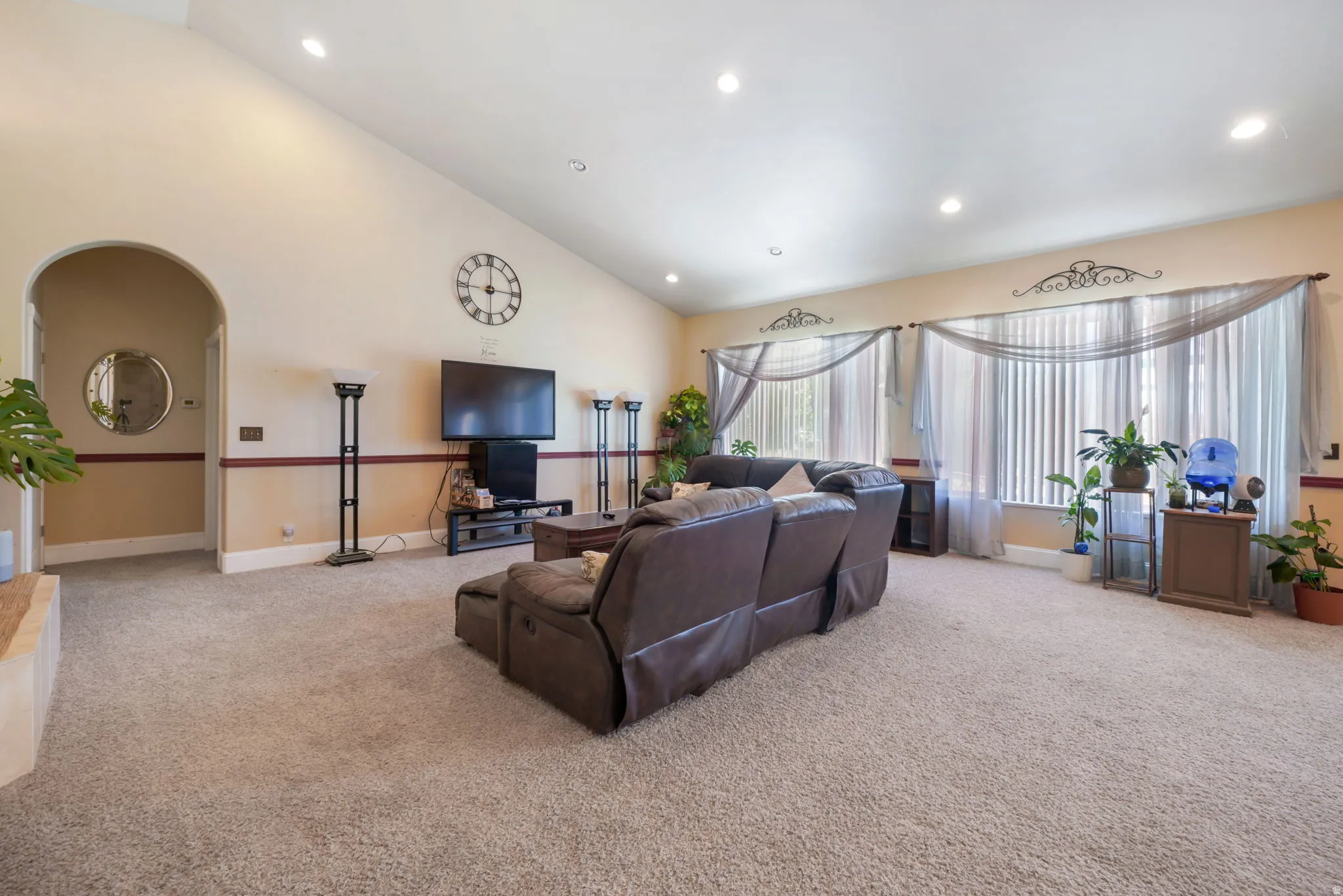 HUGE Great Room with Vaulted ceilings, recessed lighting, archway entry to primary bedroom, and broad windows with vertical blinds