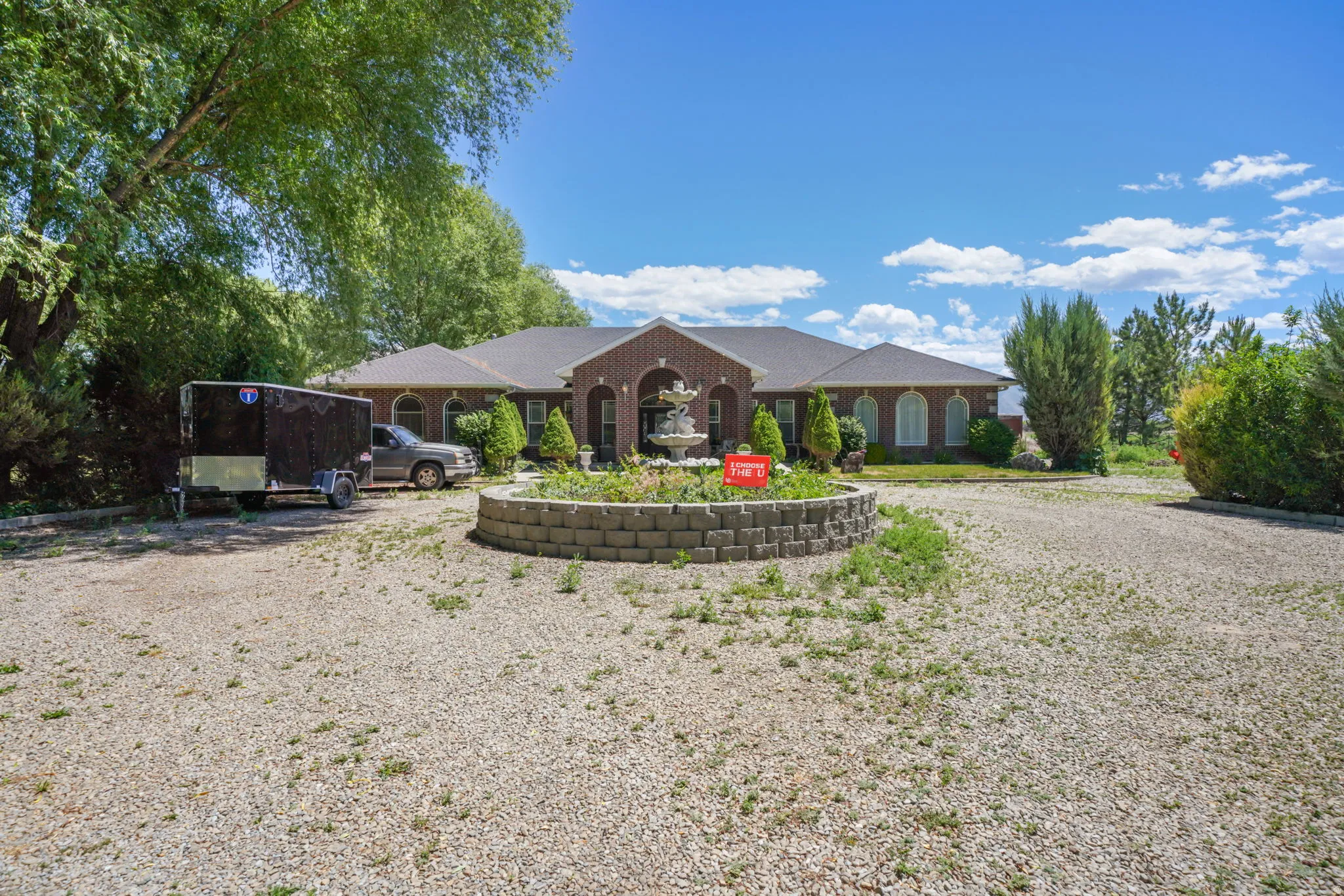 Front yard with expansive gravel driveway providing ample parking, complemented by a central stone-faced planter with a swan water feature
