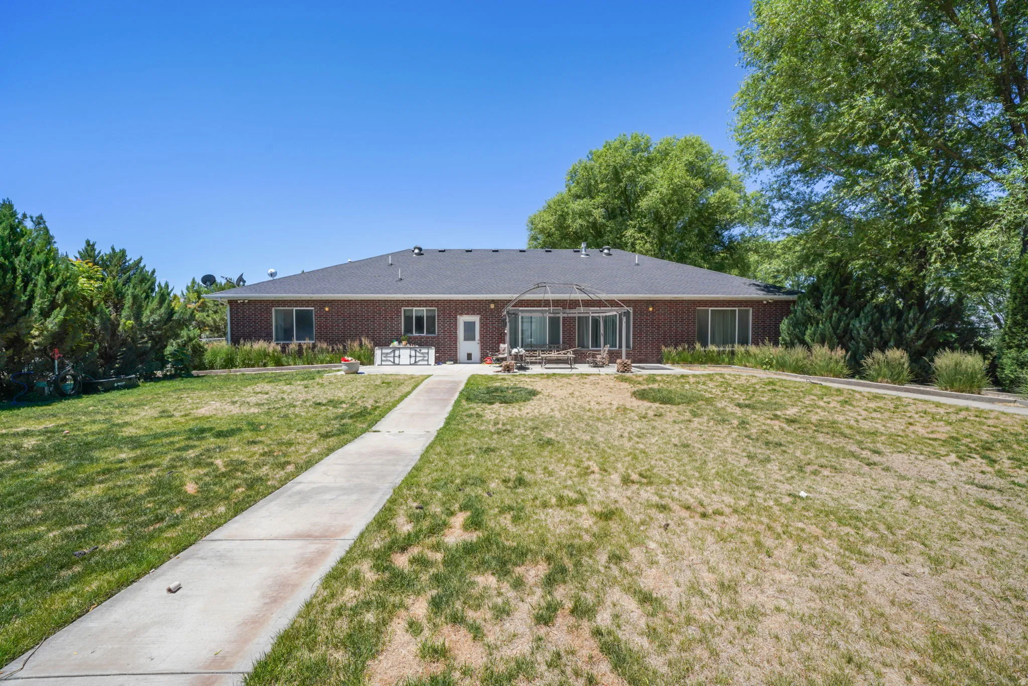 Back yard brick exterior with multiple windows, a rear patio, and a gazebo structure, complemented by mature trees and a concrete pathway