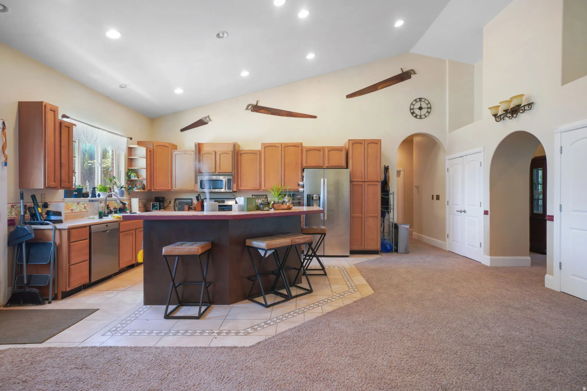 Vaulted ceiling kitchen area with stainless steel appliances, a central island with bar seating, and recessed lighting