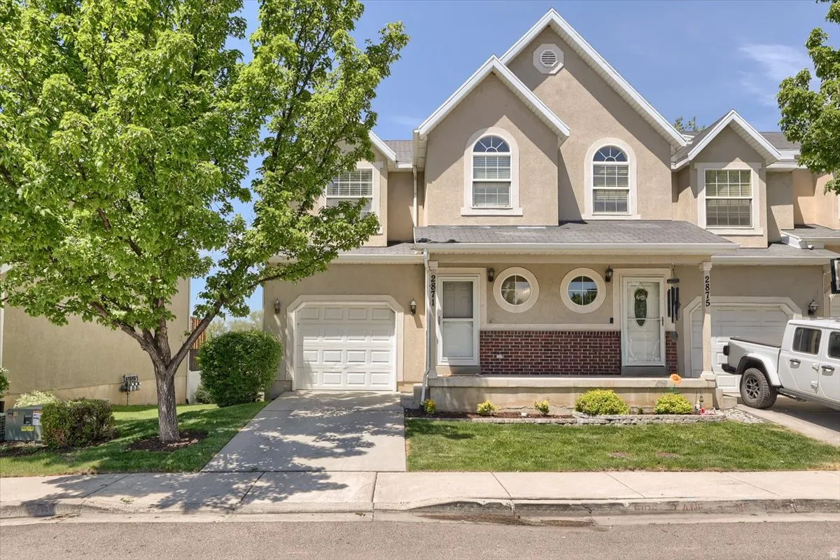 Stucco exterior featuring arched and circular windows, an attached garage, and a covered entry porch with brick detailing