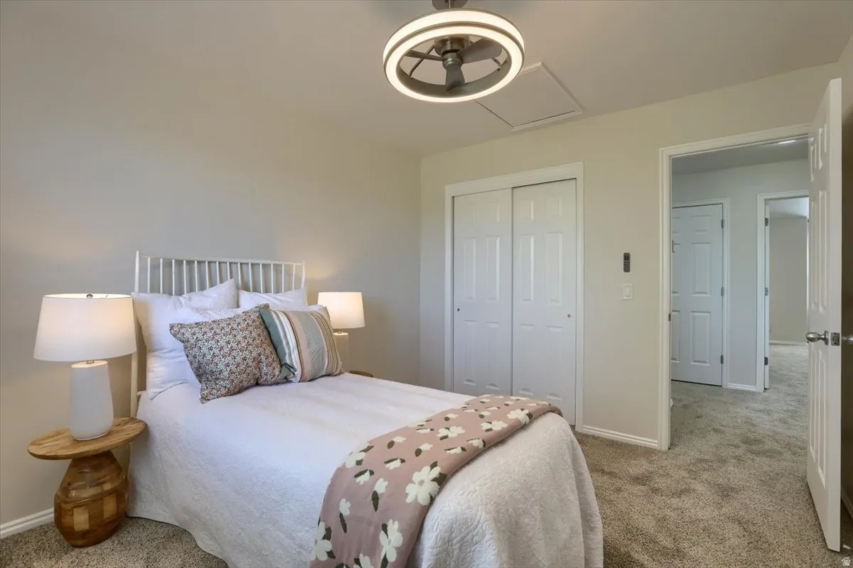 Bedroom featuring a ceiling fan with integrated lighting, textured carpet flooring, and a double-door closet with white paneled doors