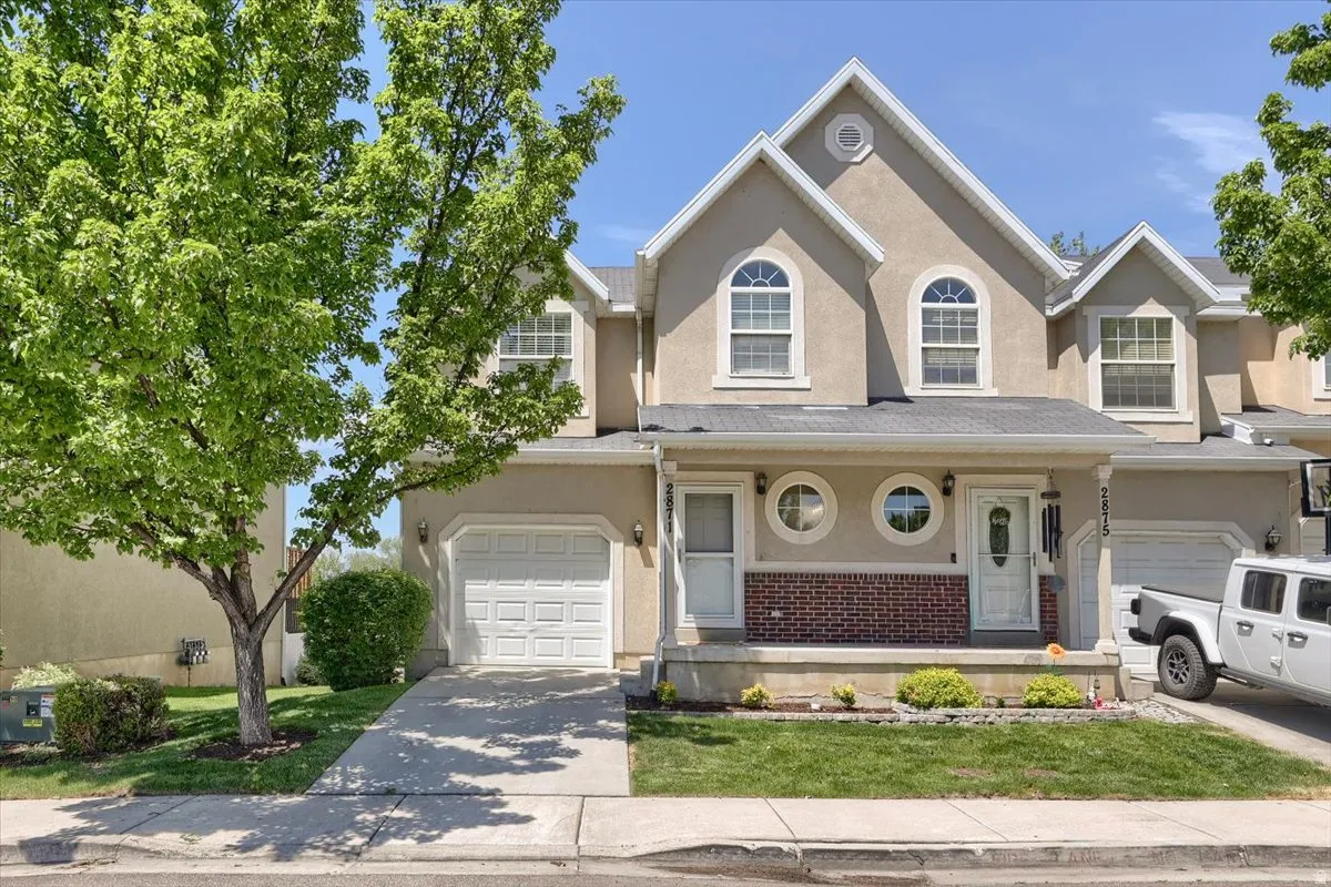 Stucco townhouse exterior featuring arched and circular windows, a covered entry with a white door, an attached garage, and a manicured lawn