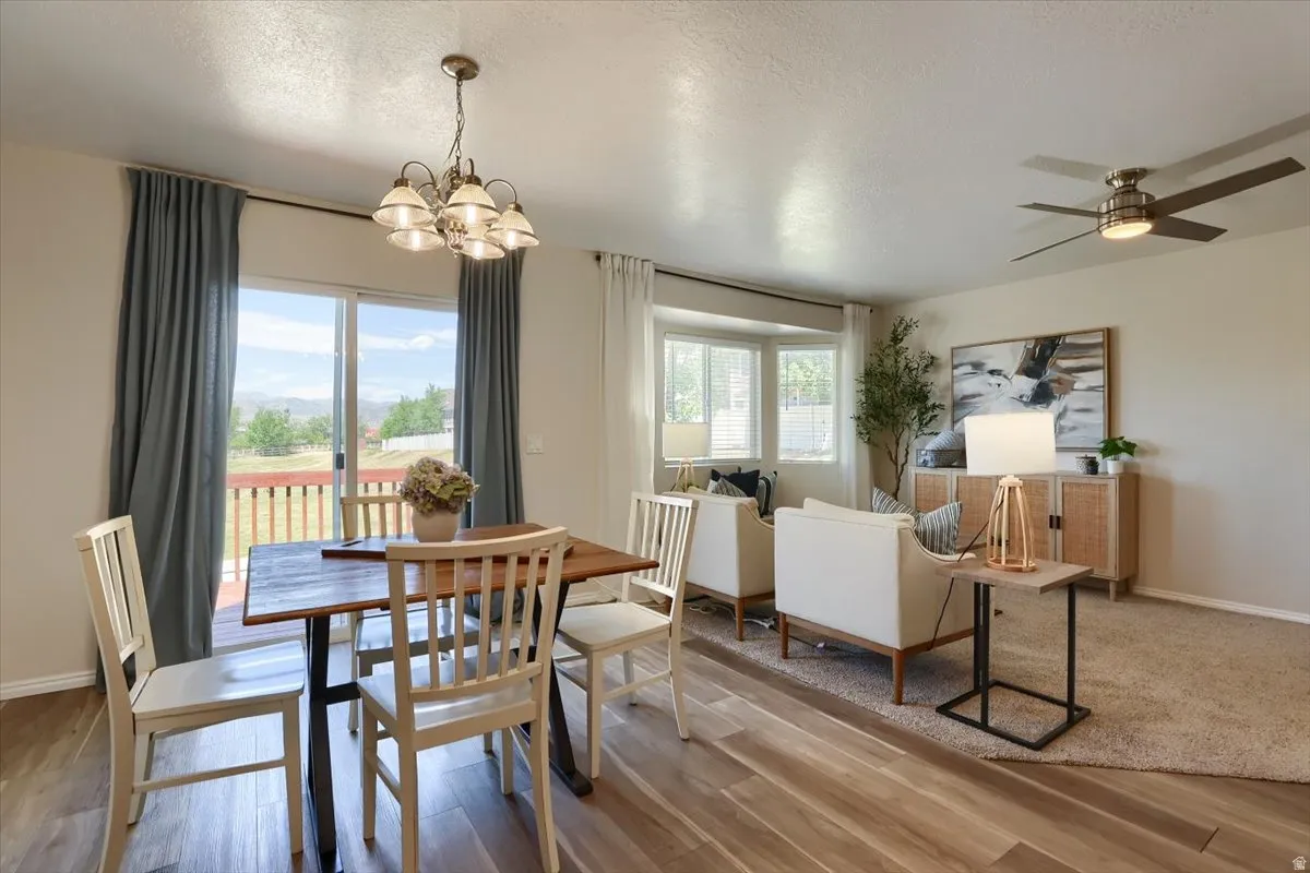 Open-concept living area featuring wood-finish flooring, a contemporary chandelier, a bay window, and a ceiling fan