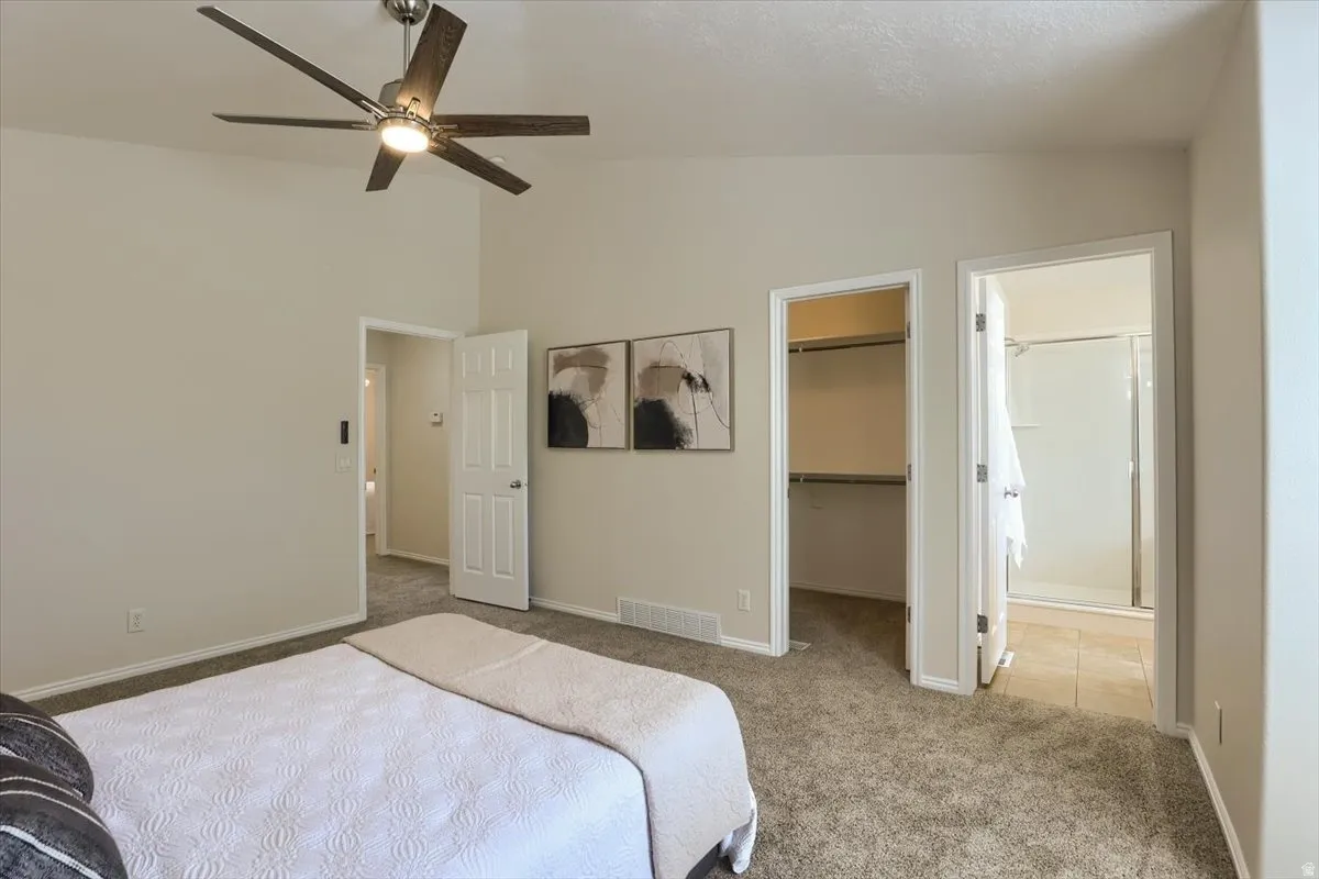 Carpeted interior room featuring vaulted ceilings with a ceiling fan, a walk-in closet, and an attached bathroom with a shower and tile flooring