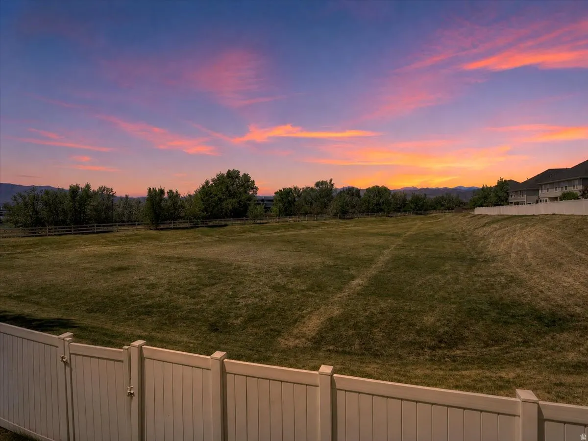 Expansive grassy lot bordered by a white privacy fence and a natural tree line, with a mountain backdrop