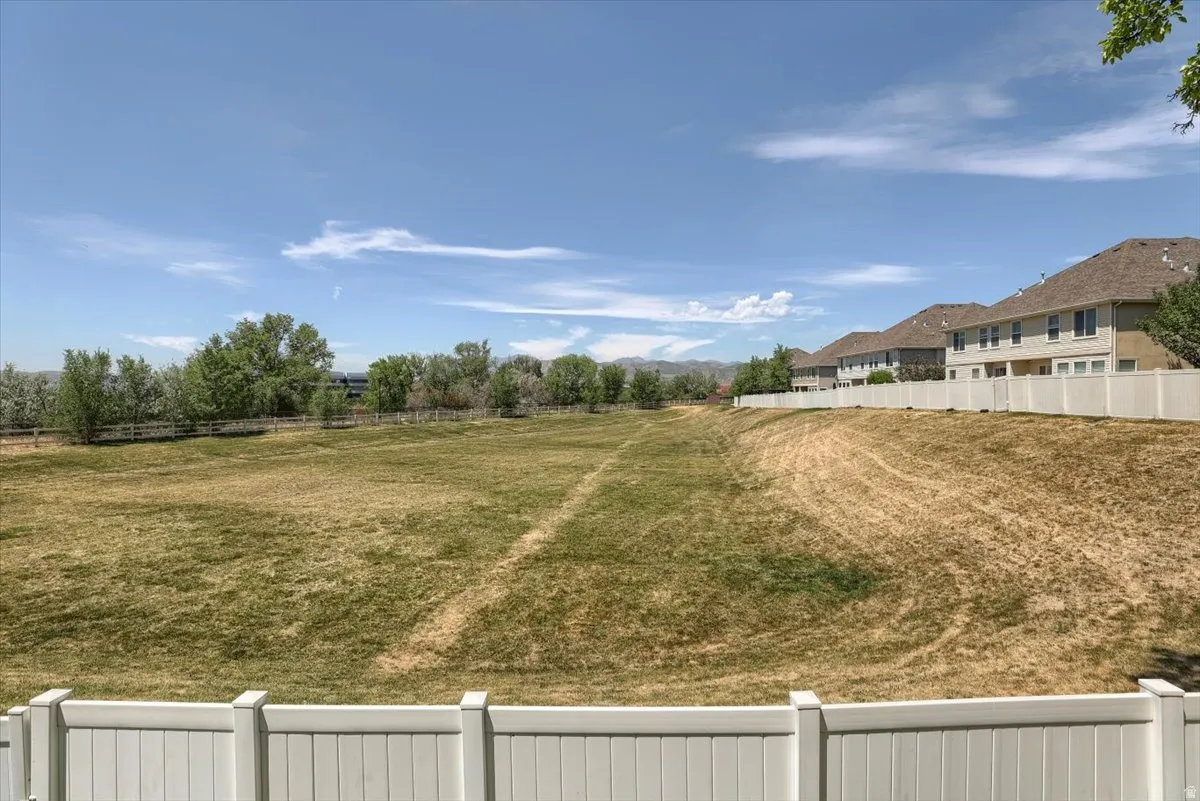 Expansive open field bordered by a white privacy fence and distant mature trees
