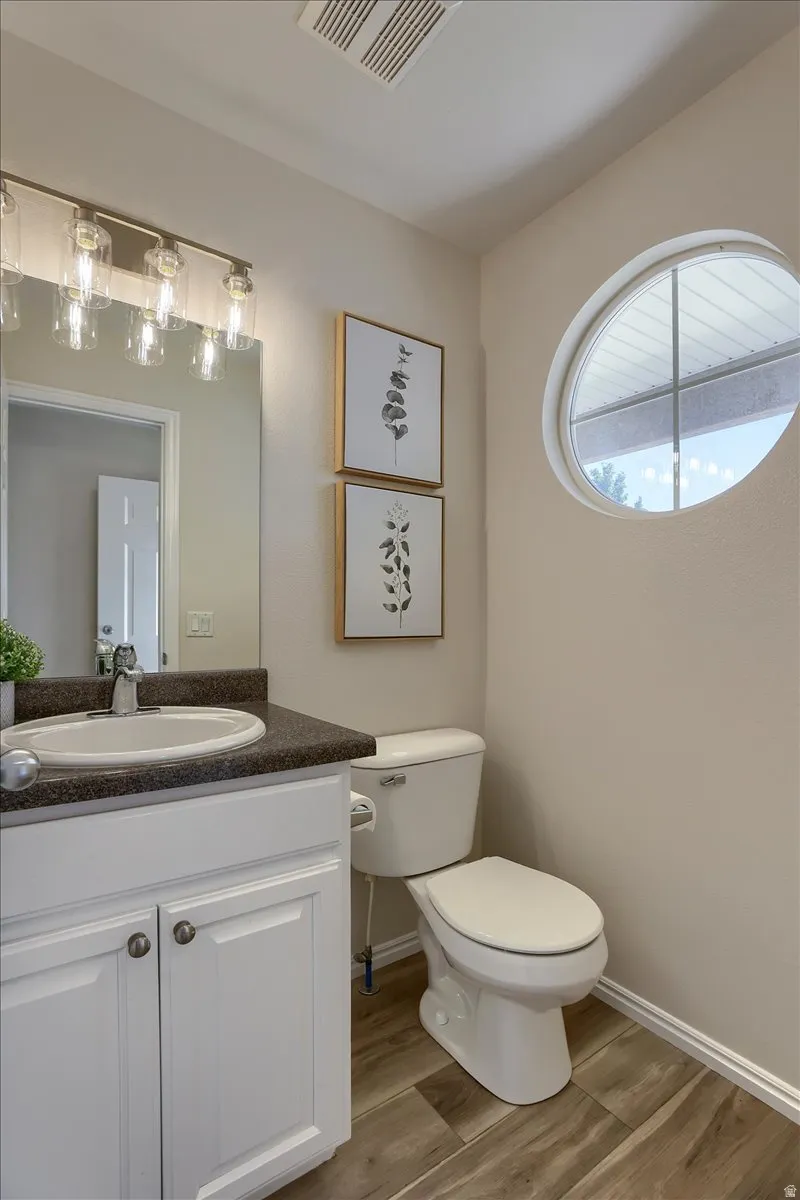 Powder room featuring a white vanity with dark countertop, wood-finish flooring, a contemporary lighting fixture, and a unique round window