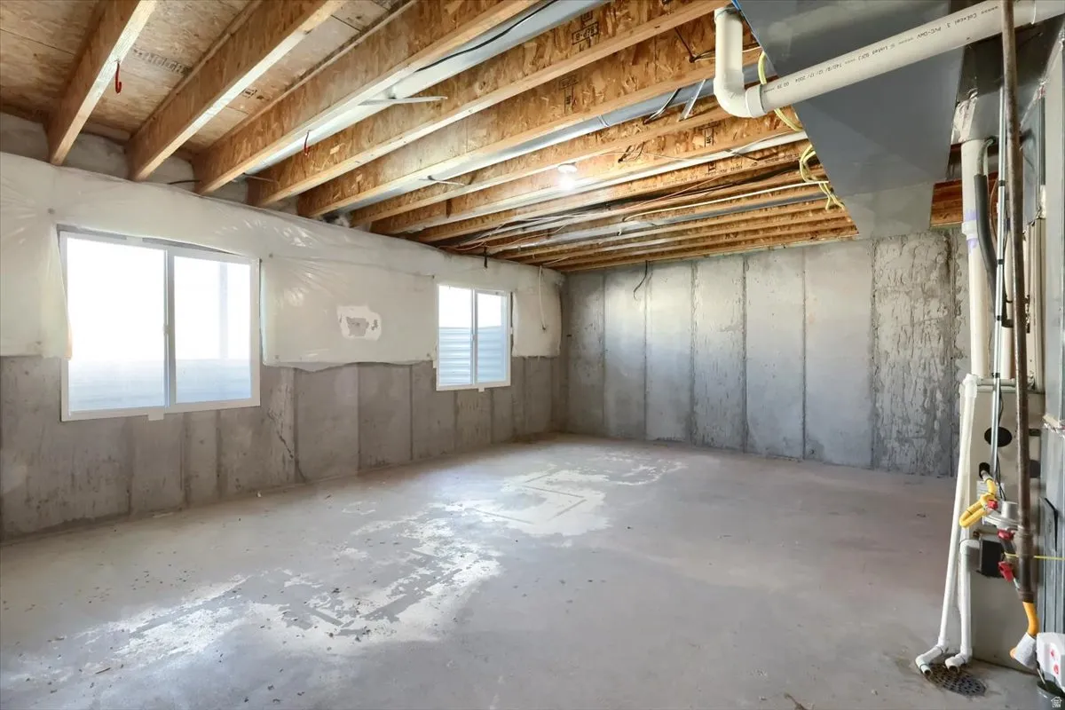 Expansive unfinished lower level featuring exposed wood joists, concrete walls, and two egress windows providing natural light