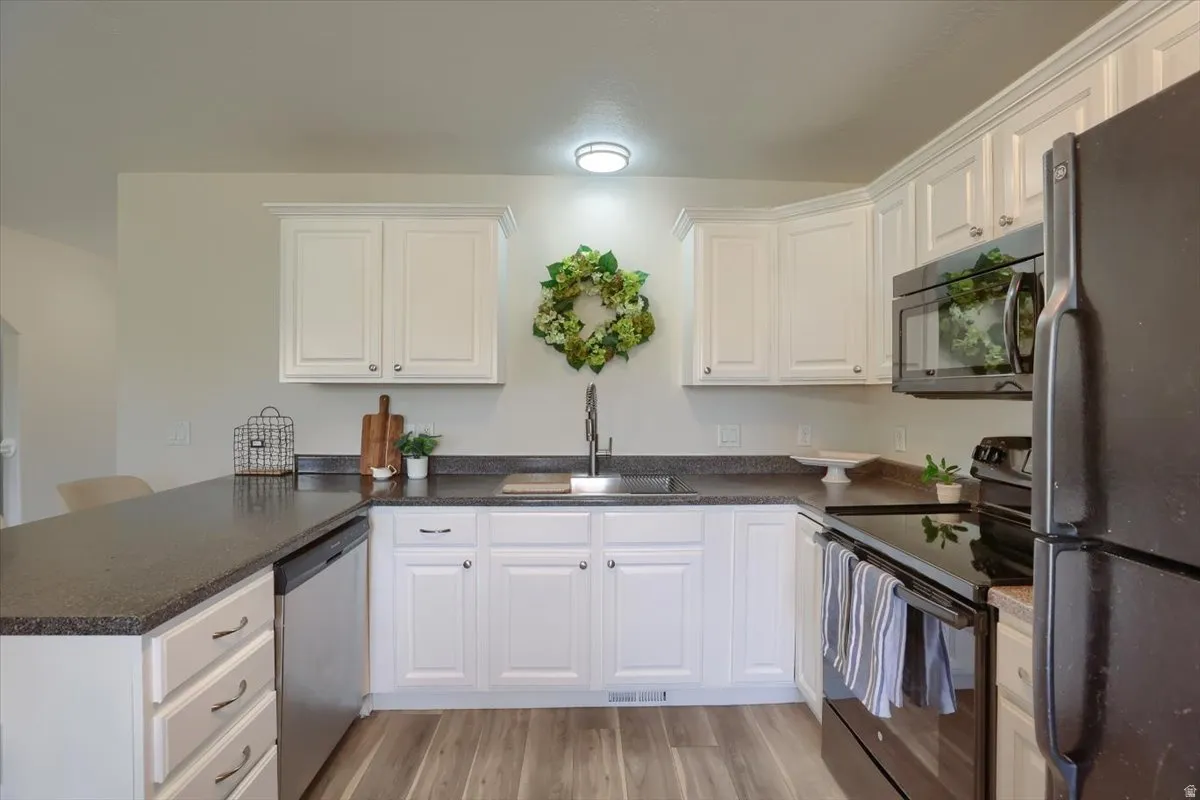 Kitchen featuring wood-finish flooring, white cabinetry, dark countertops, a stainless steel dishwasher, and black appliances including a range and microwave