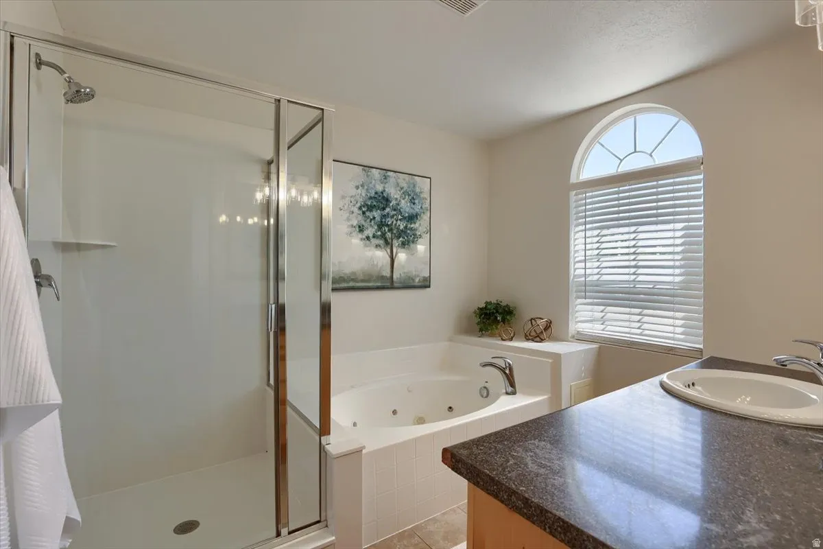 Bathroom featuring a glass-enclosed shower, built-in jetted tub, arched window with horizontal blinds, and a vanity with a dark speckled countertop and undermount sink
