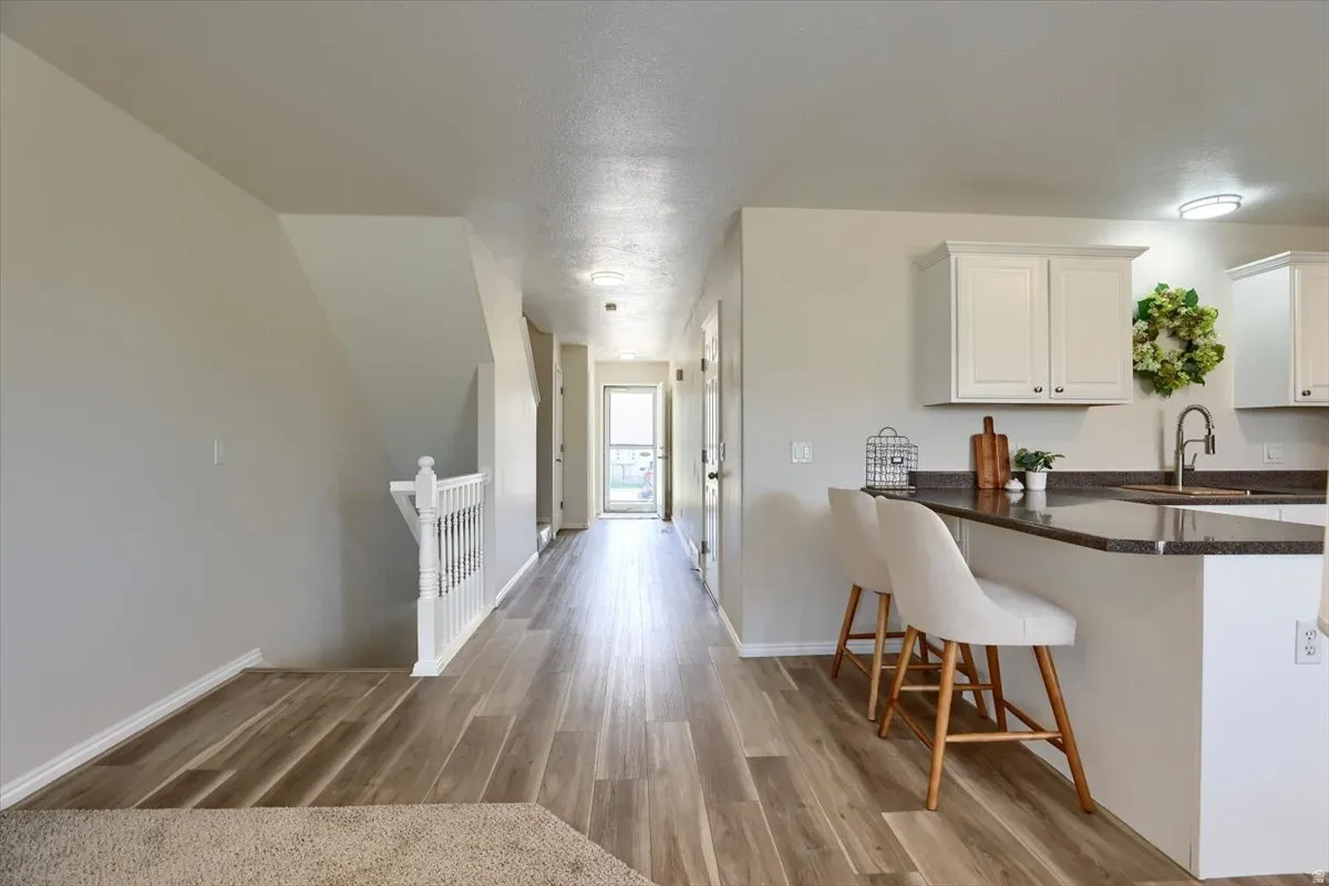 Open-concept living space featuring wood-finish flooring, white cabinetry, a built-in kitchen island with seating, and recessed ceiling lighting