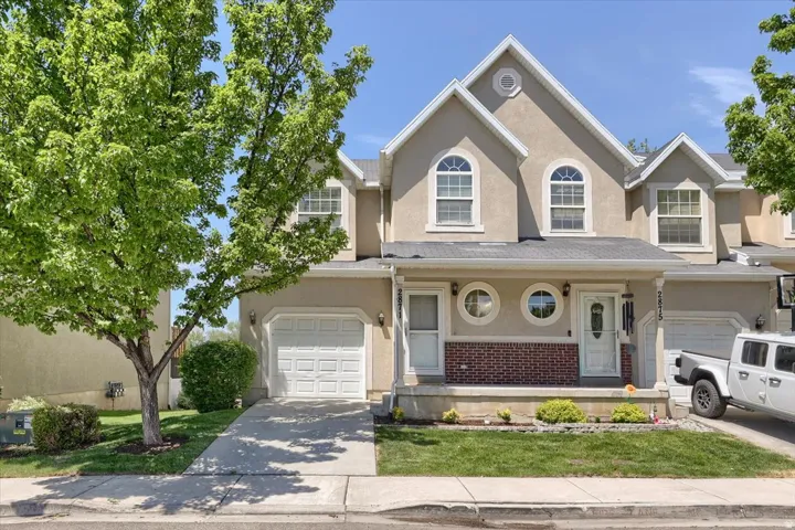 Stucco townhouse exterior featuring arched and circular windows, a covered entry with a white door, an attached garage, and a manicured lawn