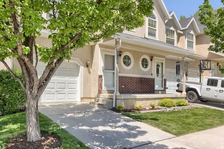 Stucco exterior with brick accent, inviting front porch, attached garage, and mature landscaping