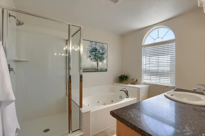 Bathroom featuring a glass-enclosed shower, built-in jetted tub, arched window with horizontal blinds, and a vanity with a dark speckled countertop and undermount sink