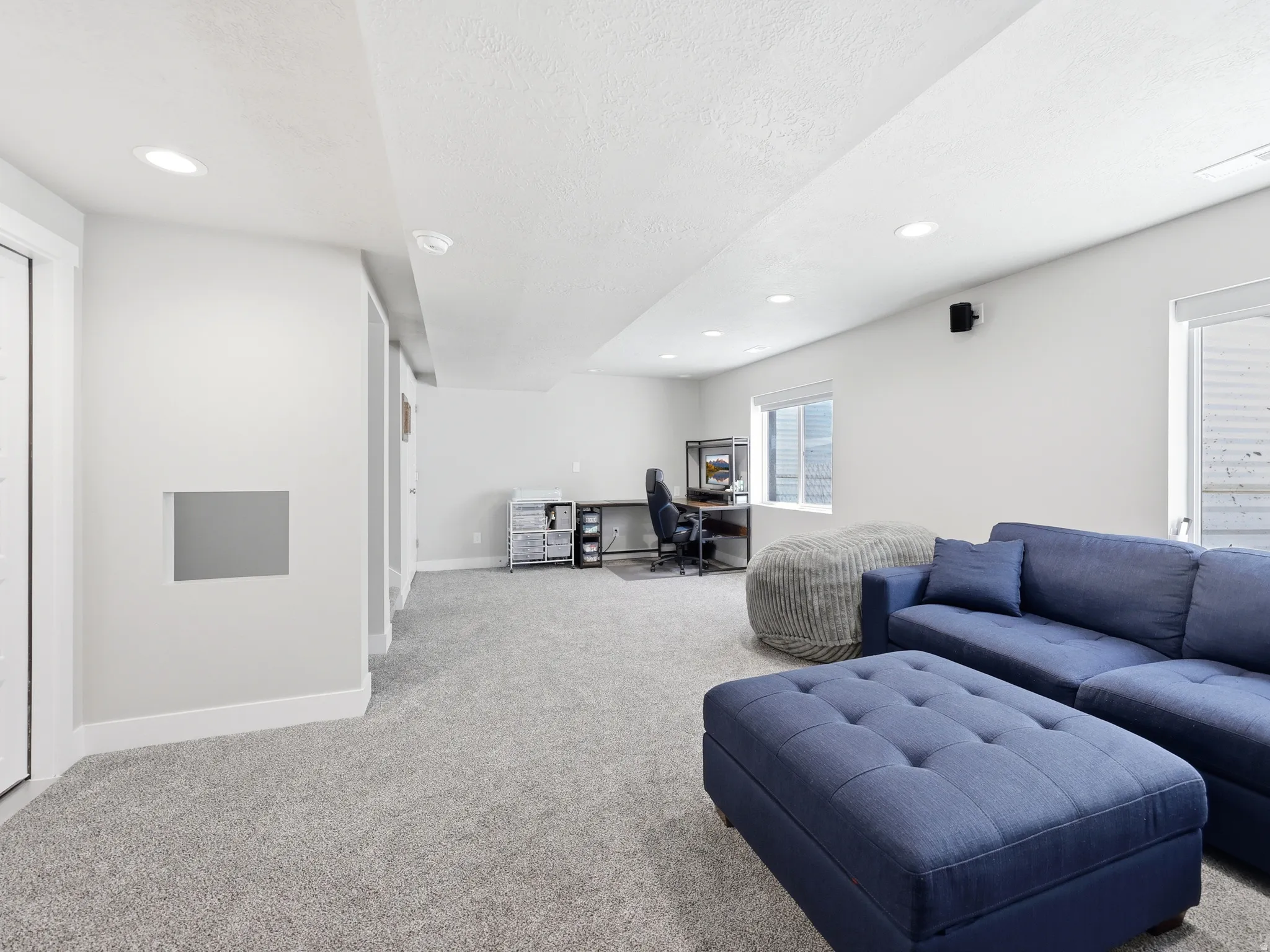 Spacious finished room featuring light gray carpeting, recessed ceiling lighting, two windows, and a built-in shelf opening