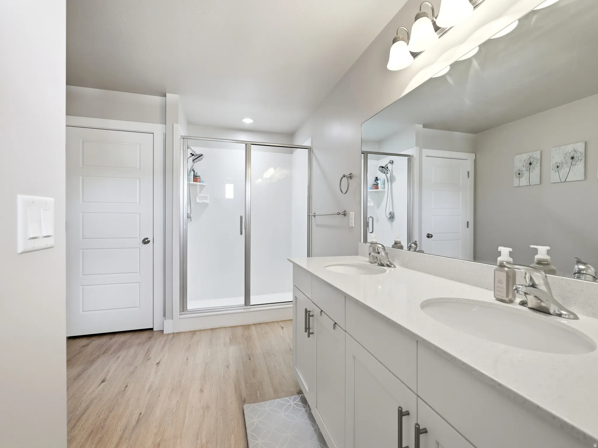 Bathroom featuring a dual vanity with undermount sinks and chrome faucets, a large mirror, and a glass-enclosed shower