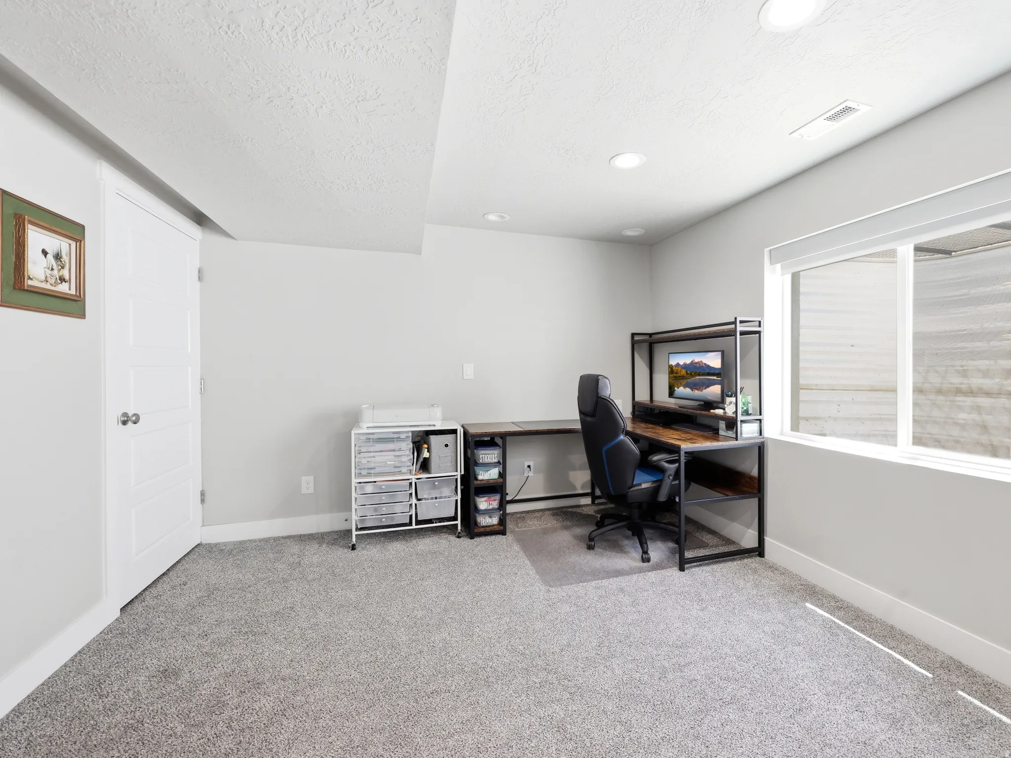 Spacious room featuring light gray carpeting, recessed lighting, and a large egress window