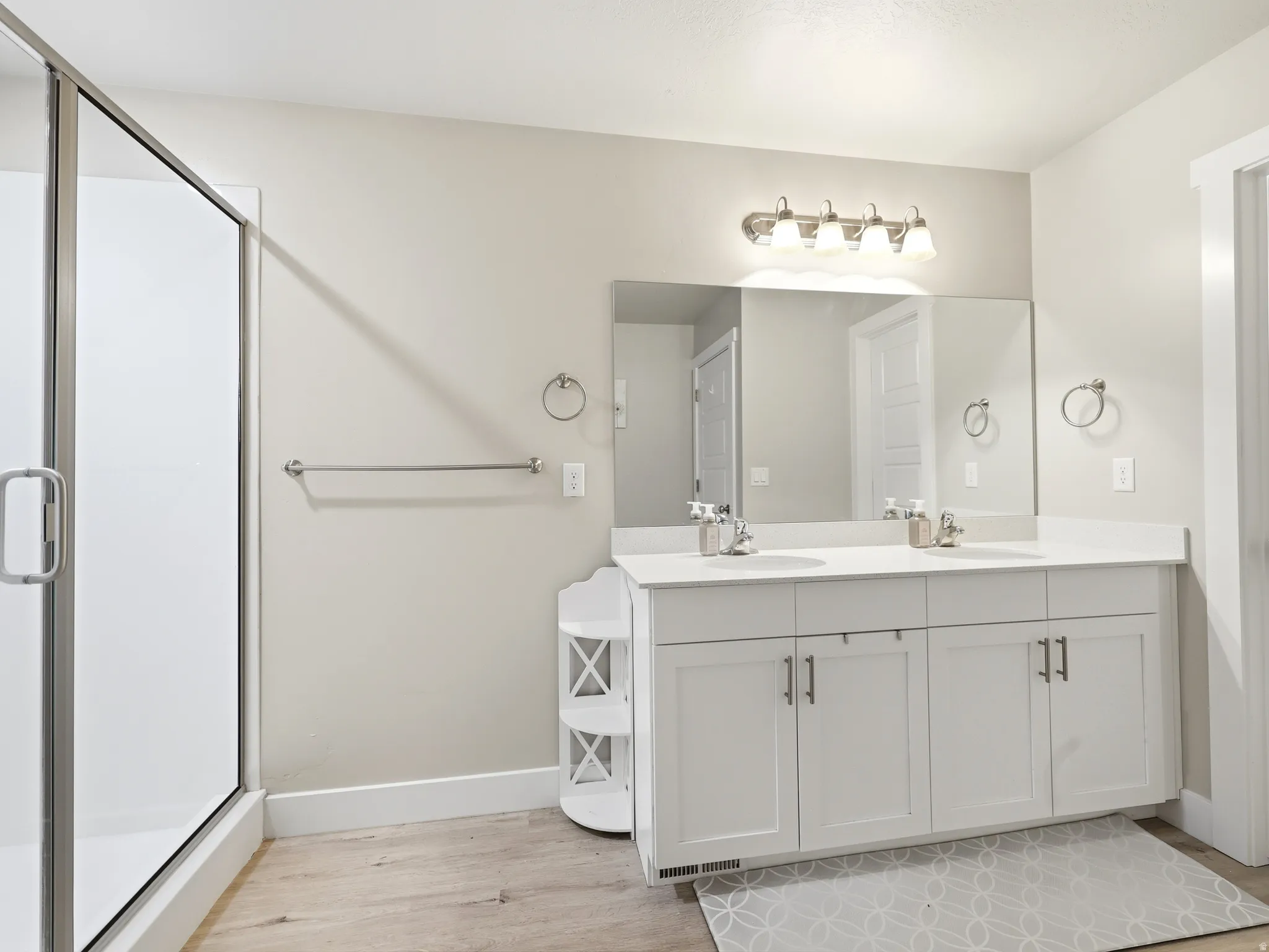 Spacious bathroom featuring a double vanity with white cabinetry and light-colored countertops, a large vanity mirror, and a glass-enclosed shower