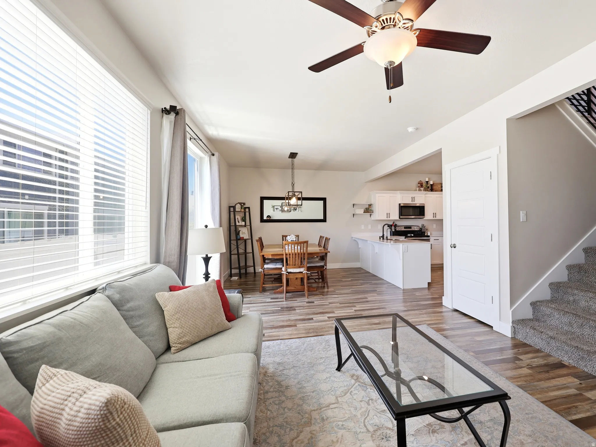 Open-concept living area featuring wood-finish flooring, a contemporary ceiling fan, and large windows with blinds