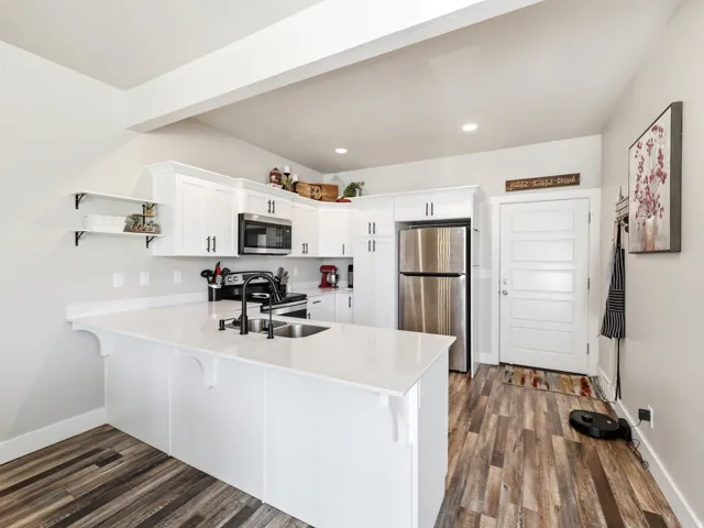 Contemporary kitchen featuring white cabinetry, a large white countertop island, stainless steel appliances, and wood-finish flooring
