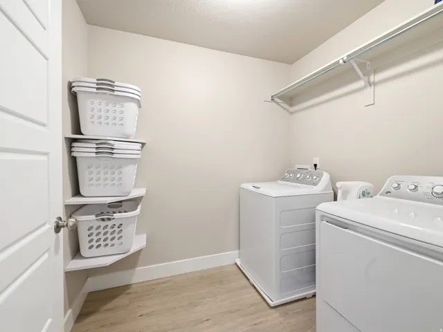 Dedicated laundry room featuring light wood-finish flooring, corner shelving, and a wall-mounted clothing rod