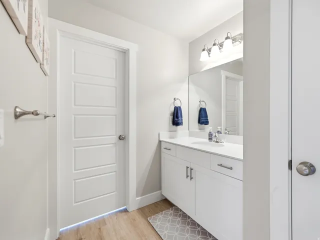 Bathroom featuring a white vanity with integrated sink, chrome faucet, wall-mounted mirror, and brushed nickel light fixture