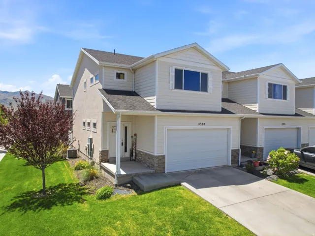 Exterior featuring beige siding, stone facade accents, a single-car garage, a covered front porch, and a well-maintained lawn