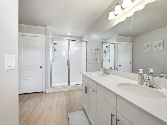 Bathroom featuring a dual vanity with undermount sinks and chrome faucets, a large mirror, and a glass-enclosed shower