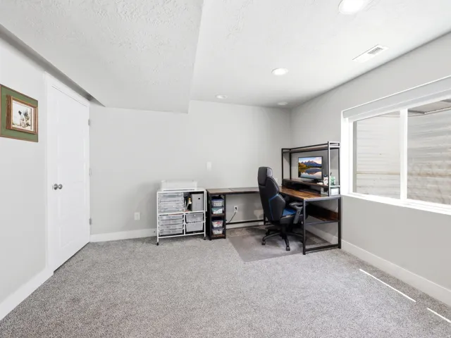 Spacious room featuring light gray carpeting, recessed lighting, and a large egress window