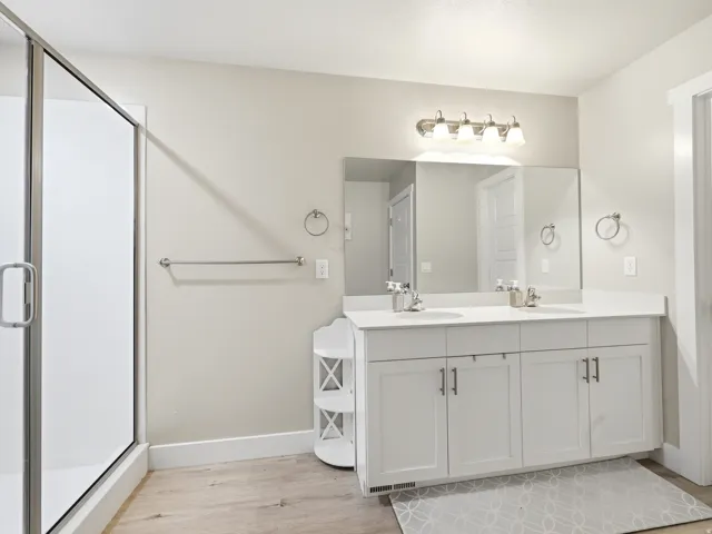 Spacious bathroom featuring a double vanity with white cabinetry and light-colored countertops, a large vanity mirror, and a glass-enclosed shower