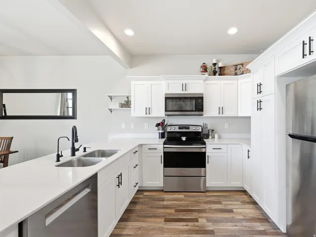 Modern kitchen featuring white shaker cabinetry, stainless steel appliances, and wood-finish flooring