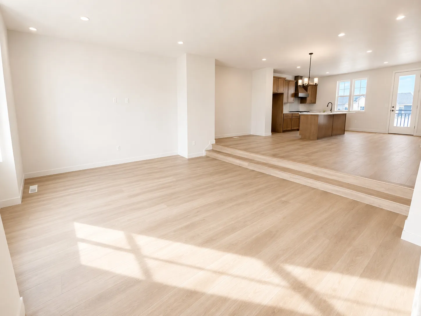 Expansive open-concept space featuring light wood-finish flooring, recessed lighting, and a tiered architectural design