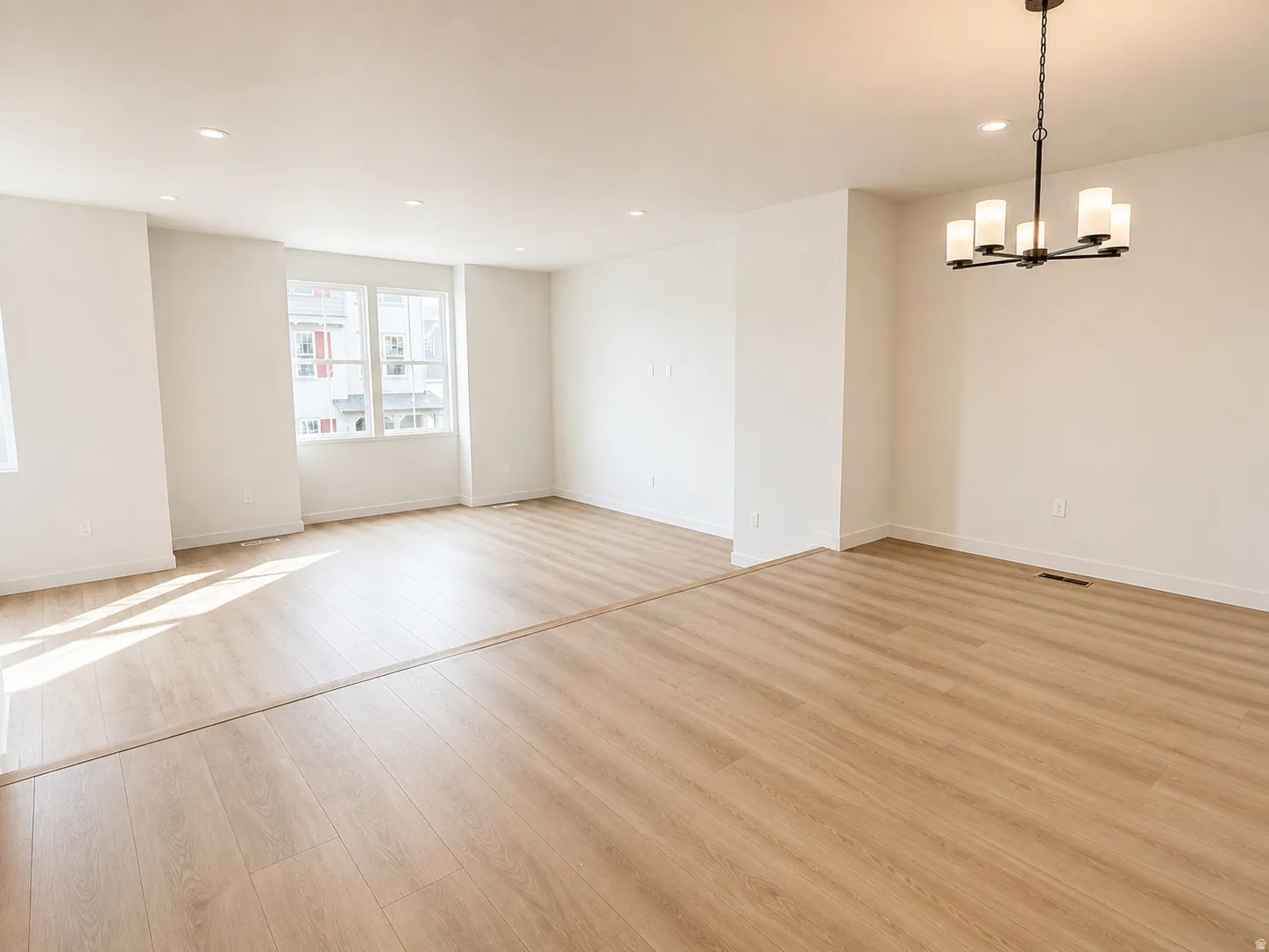 Open-concept interior featuring light wood-finish flooring, recessed ceiling lighting, and a contemporary chandelier