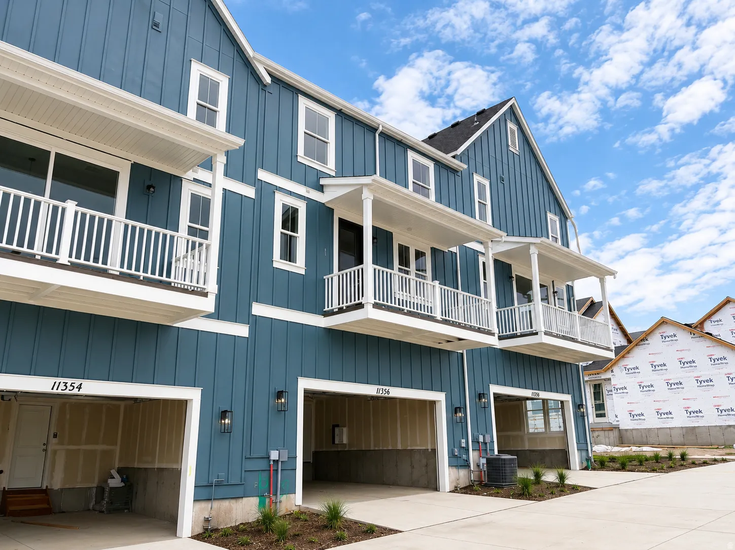 Board and batten siding, white-railed balconies, covered porches, exterior wall lanterns, and integrated single-car garages