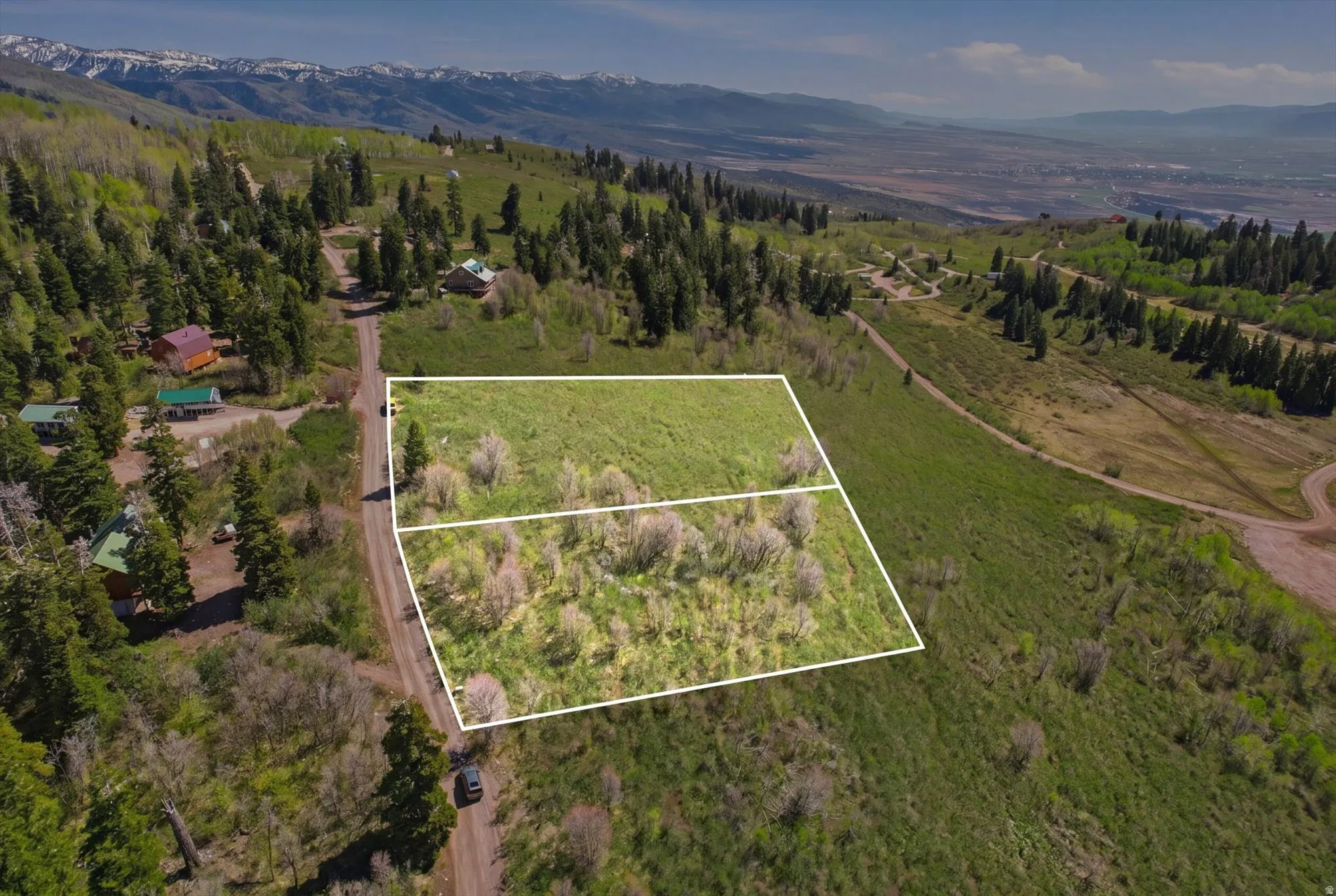 Expansive mountain property featuring two distinct parcels outlined in white, set against a backdrop of distant snow-capped peaks