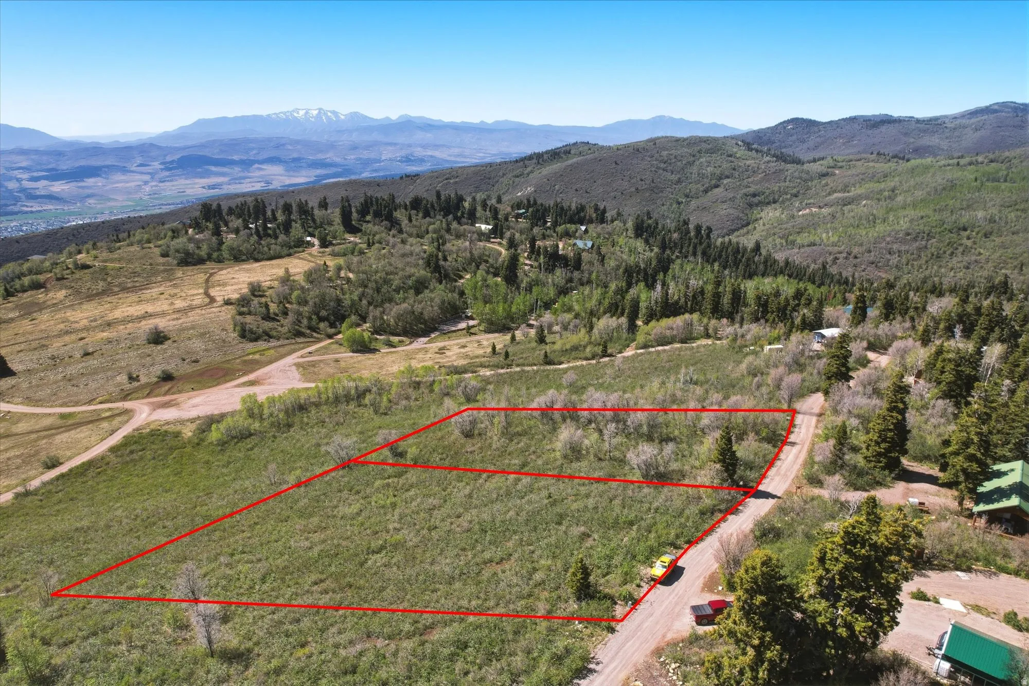 Expansive elevated land parcel outlined in red, featuring natural vegetation and surrounding mature trees