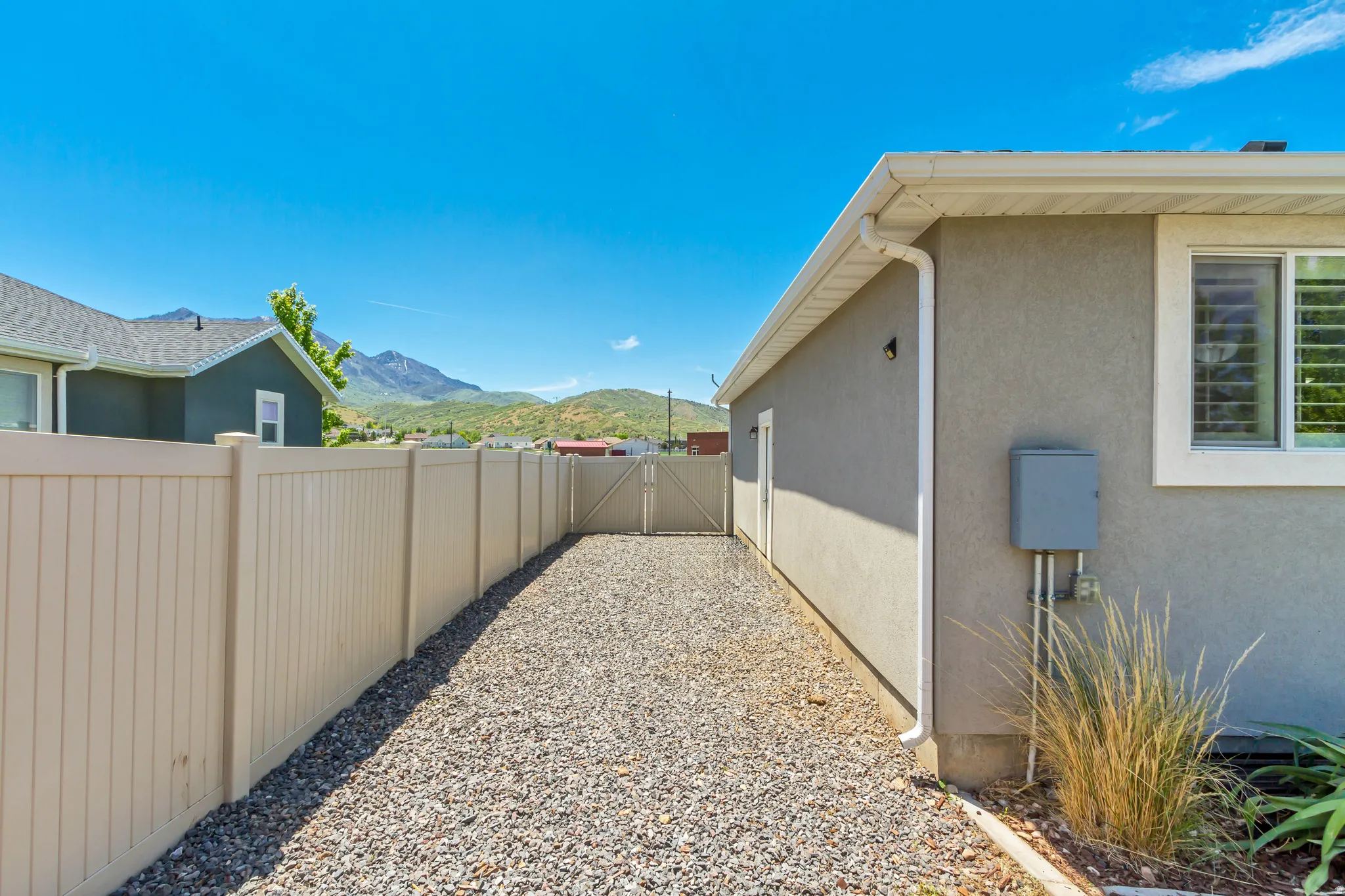 Gravel side yard featuring a light-toned privacy fence, a stucco exterior, and a white-framed window with interior shutters