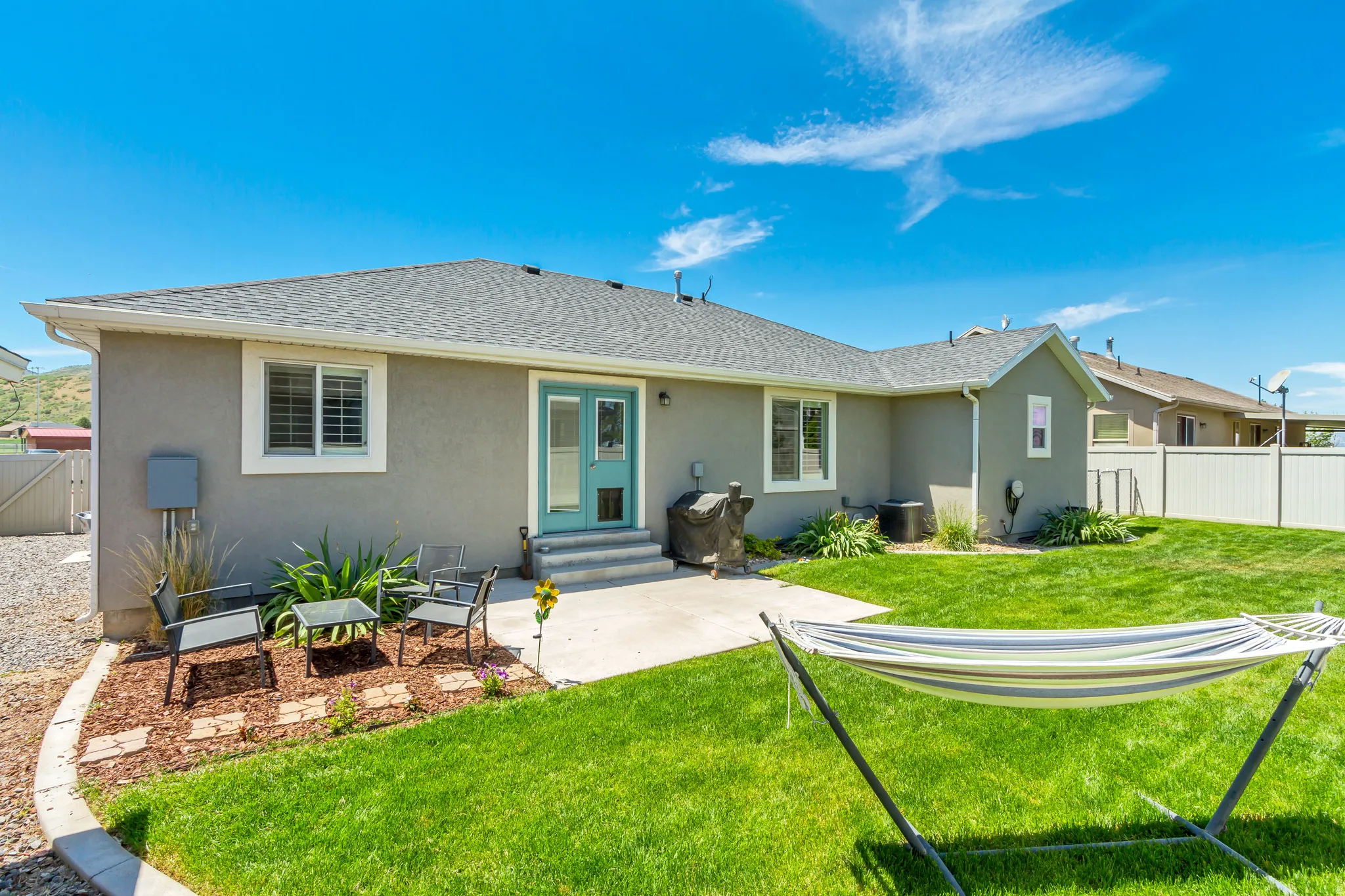 Exterior stucco finish with a teal patio door, concrete patio, and a landscaped garden bed