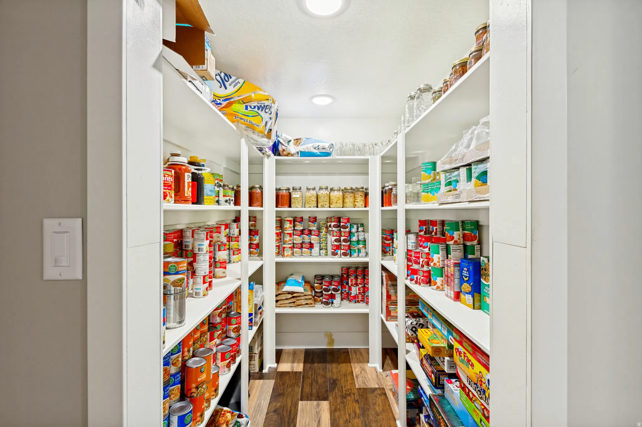 Walk-in pantry featuring extensive built-in shelving, recessed ceiling lighting, and wood-finish flooring