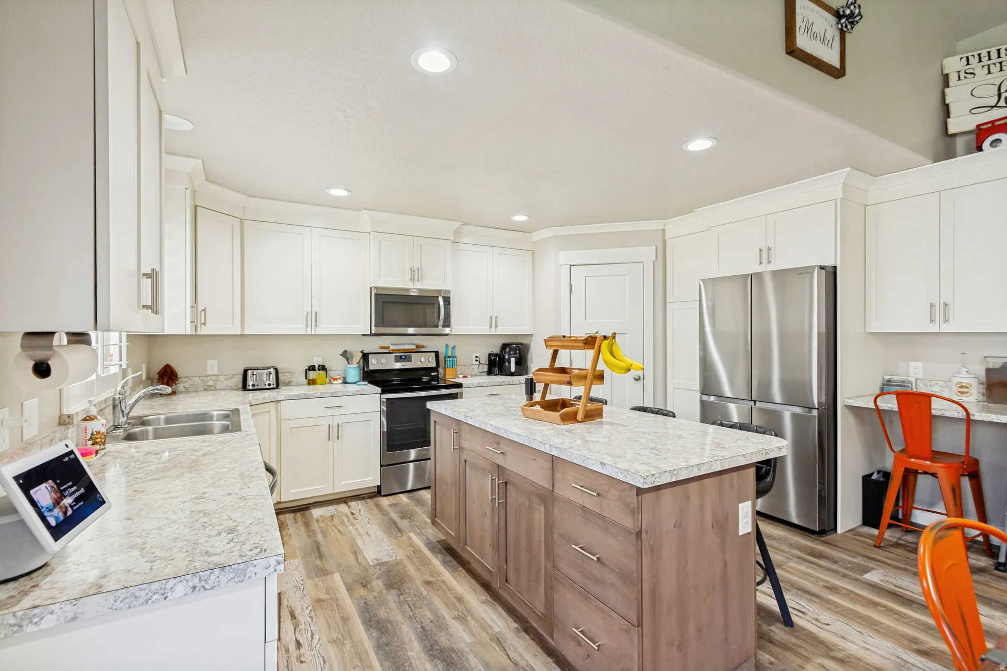 Modern kitchen featuring white cabinetry, a central island with wood-finish base, stainless steel appliances, and wood-finish flooring