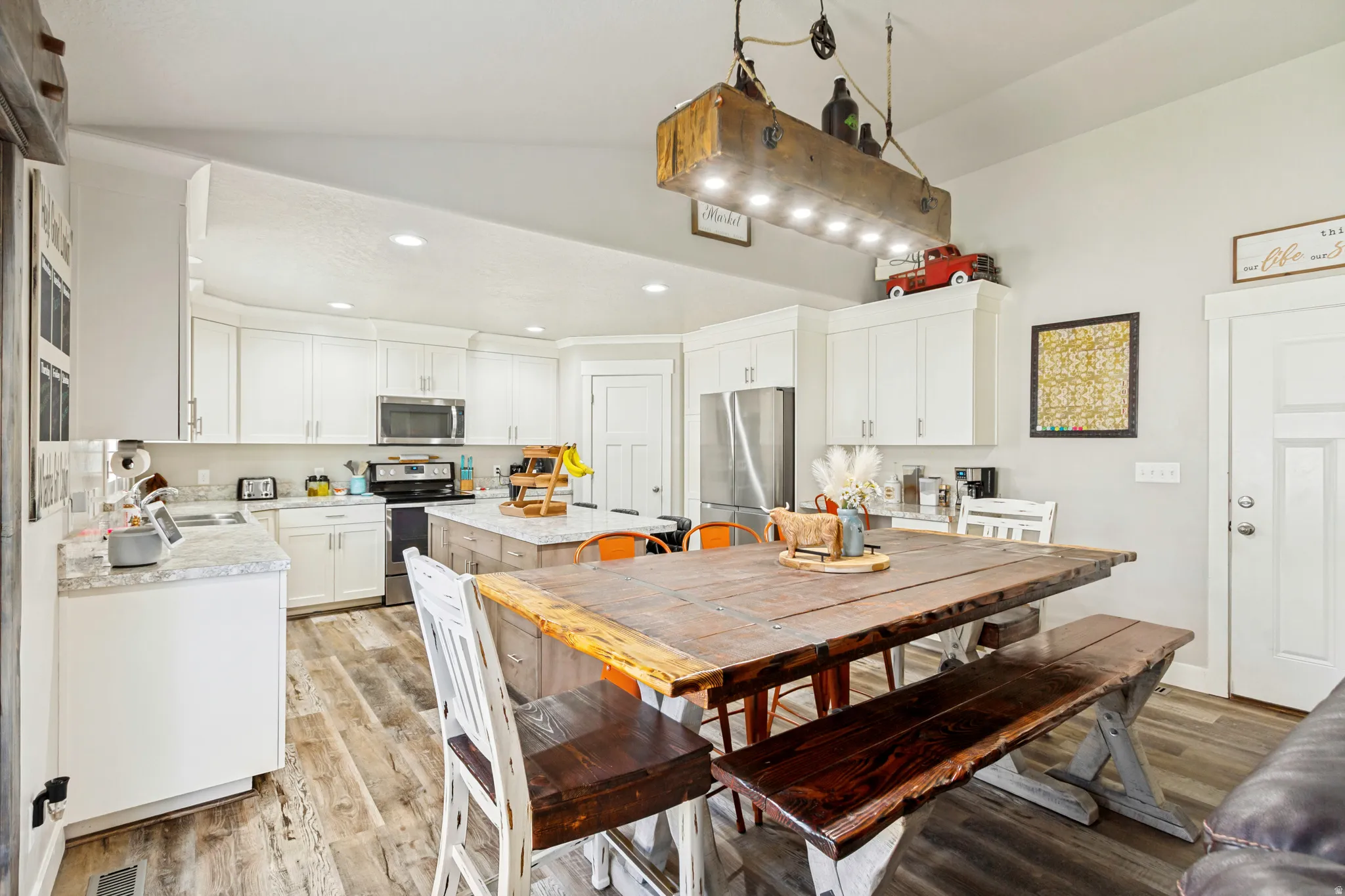 Open-concept kitchen and dining area featuring light wood-finish flooring, white cabinetry, stainless steel appliances, and recessed lighting