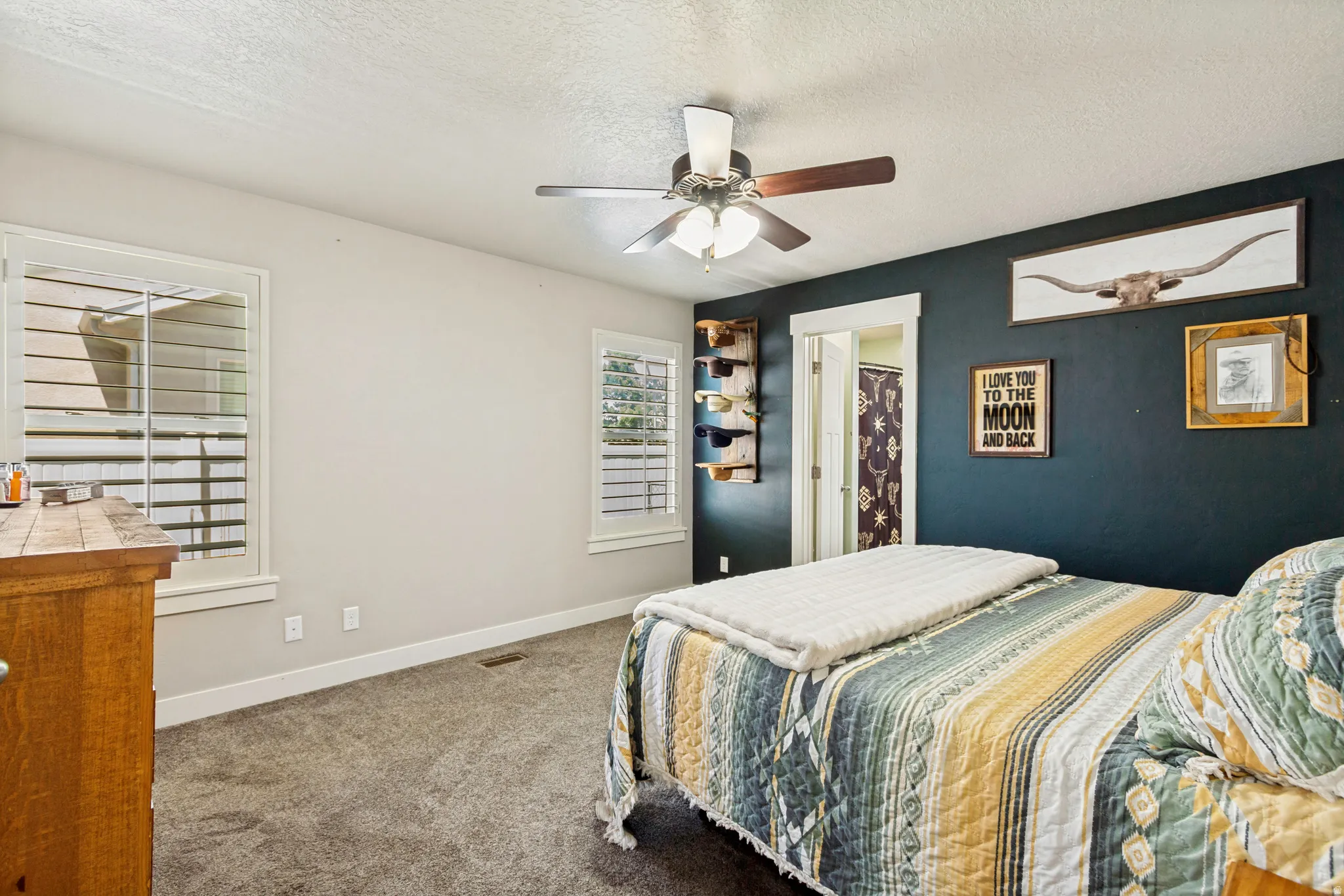 Spacious room featuring plush carpeting, two windows with louvered shutters, and a ceiling fan with integrated lighting
