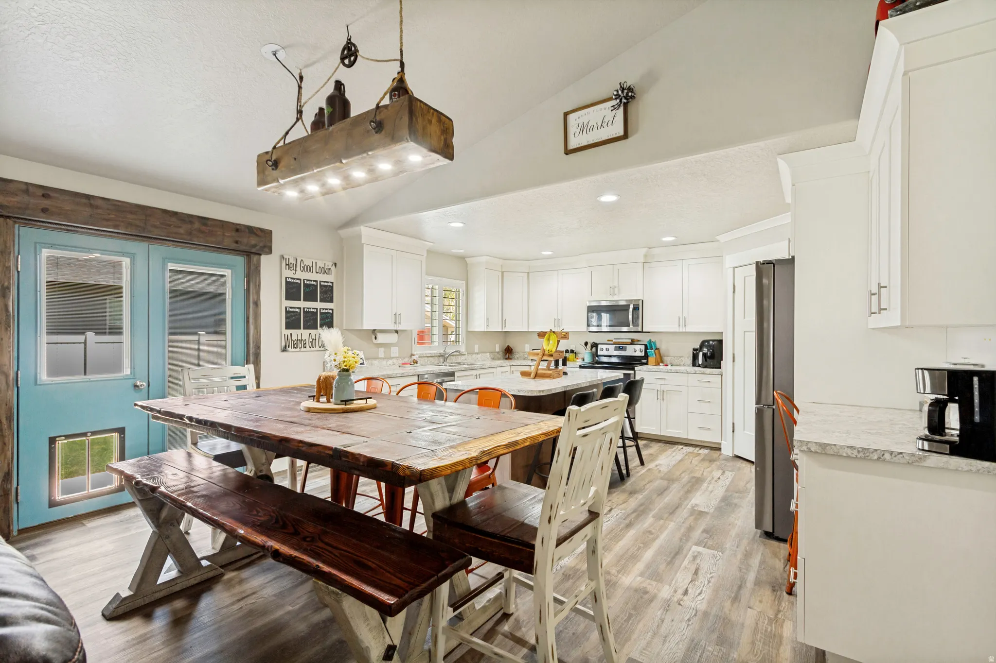 Spacious kitchen and dining area featuring a vaulted ceiling with an industrial-style light fixture, white cabinetry, a kitchen island with seating, and wood-finish flooring