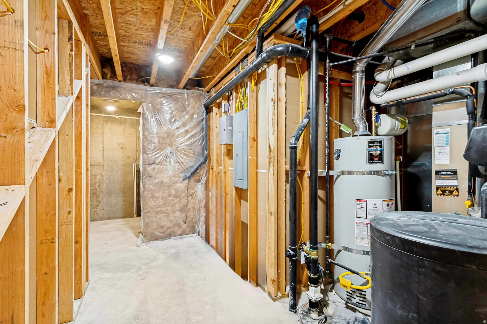 Unfinished basement area featuring exposed wood framing, concrete flooring, and visible utility infrastructure including a water heater and electrical panels
