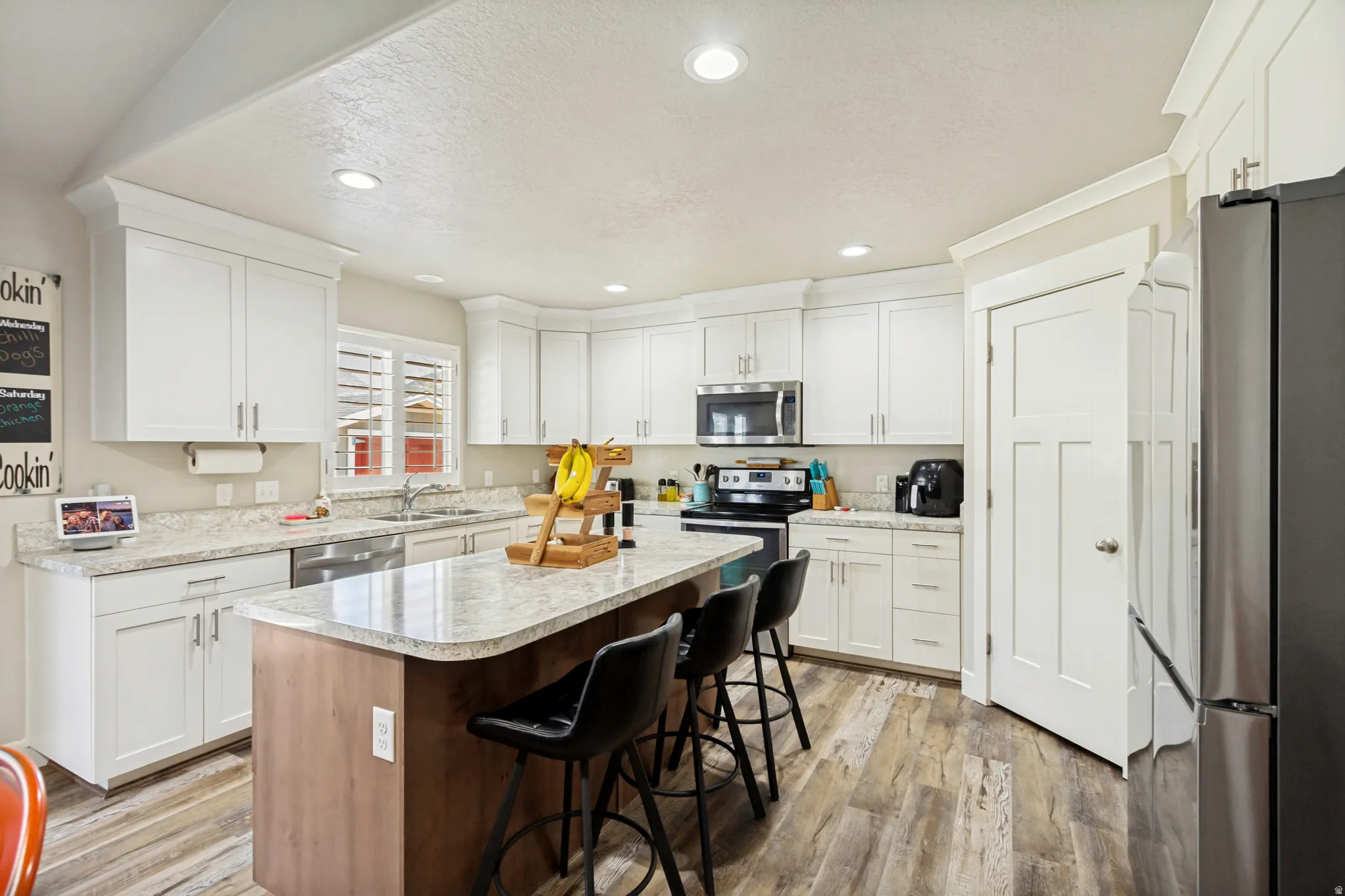 Kitchen featuring white shaker-style cabinetry, light-toned countertops, a central island with wood-finish paneling, and stainless steel appliances