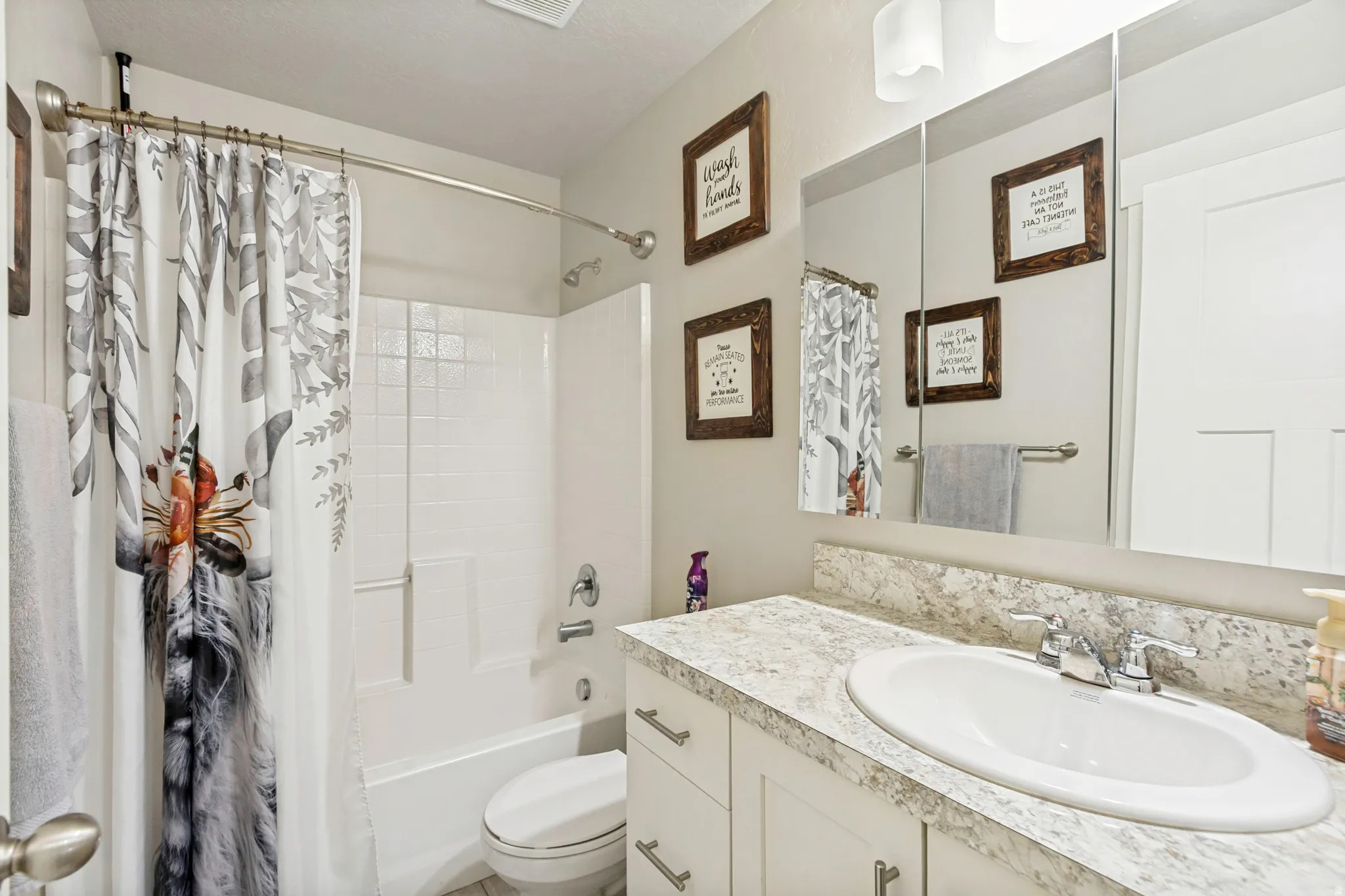 Bathroom featuring a single vanity with a laminate countertop and an integrated sink, a large wall-mounted mirror, and a shower-over-tub combination with white subway tile surround