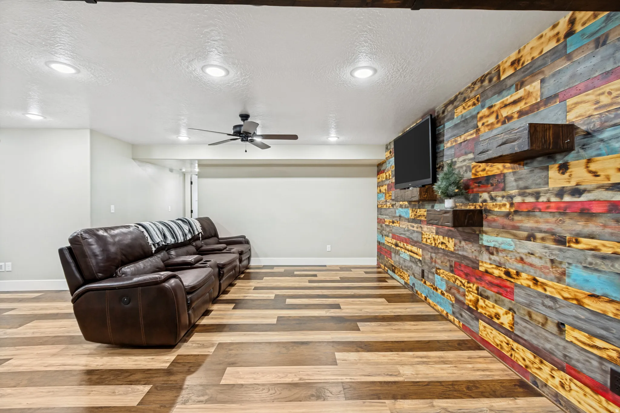 Accent wall with multi-toned wood paneling, featuring integrated floating shelves and a wall-mounted television