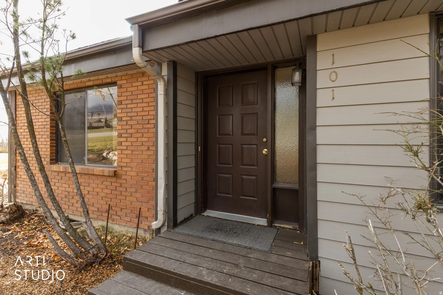 Exterior entryway featuring a paneled door, sidelight, wall-mounted light fixture, and address numbers